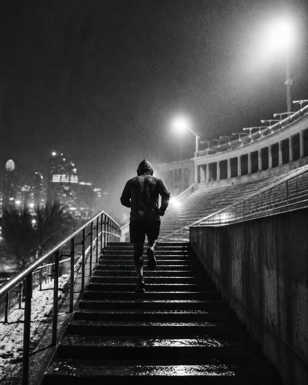 An athlete running up wet stadium stairs at night.